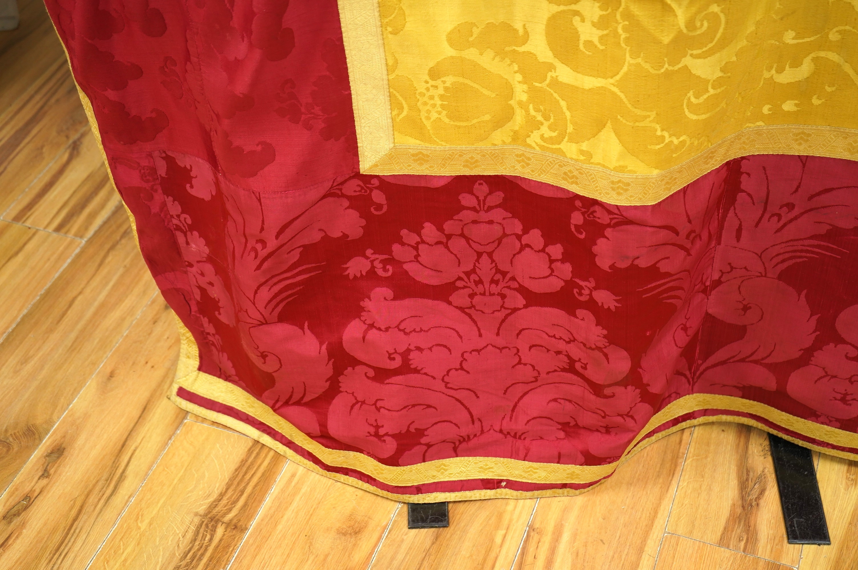 A 19th century gold and crimson silk damask bed cover, the centre being short loom widths of gold damask in a large repeating design, the outer panel a similar crimson damask, both finished with decorative gold braid bor